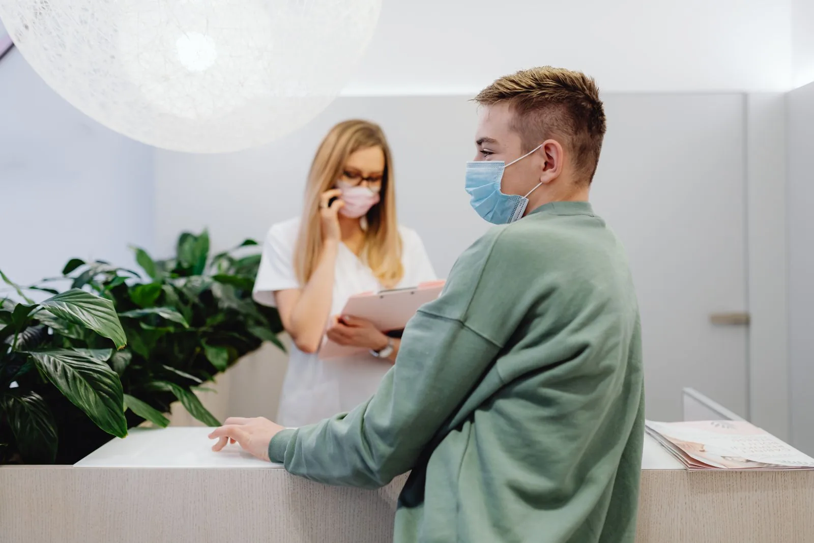 Un paziente e un receptionist in una clinica che indossano mascherine, garantendo la sicurezza sanitaria.
